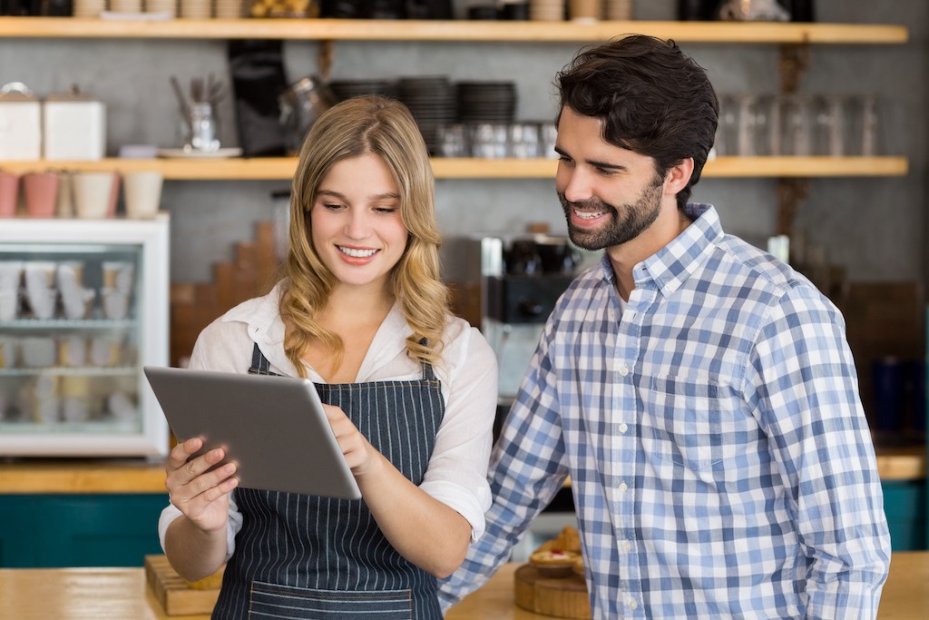 Smiling man and waitress standing at counter using digital tablet in cafe